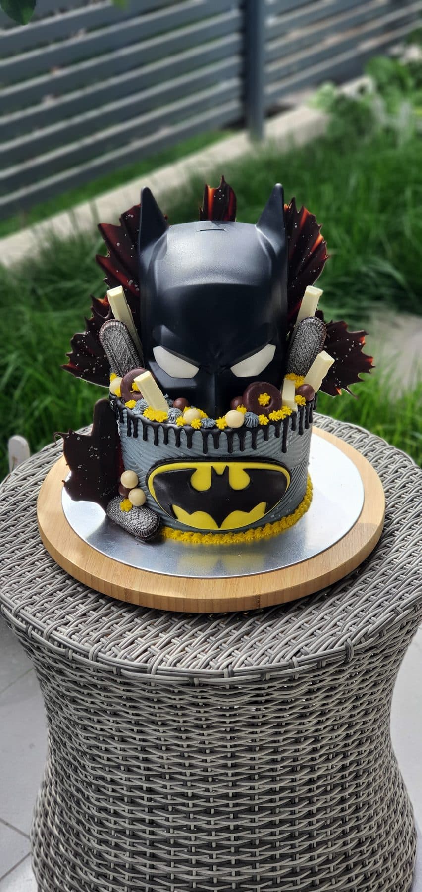 Tarta temática de Batman con máscara negra, logo amarillo y decoraciones de chocolate